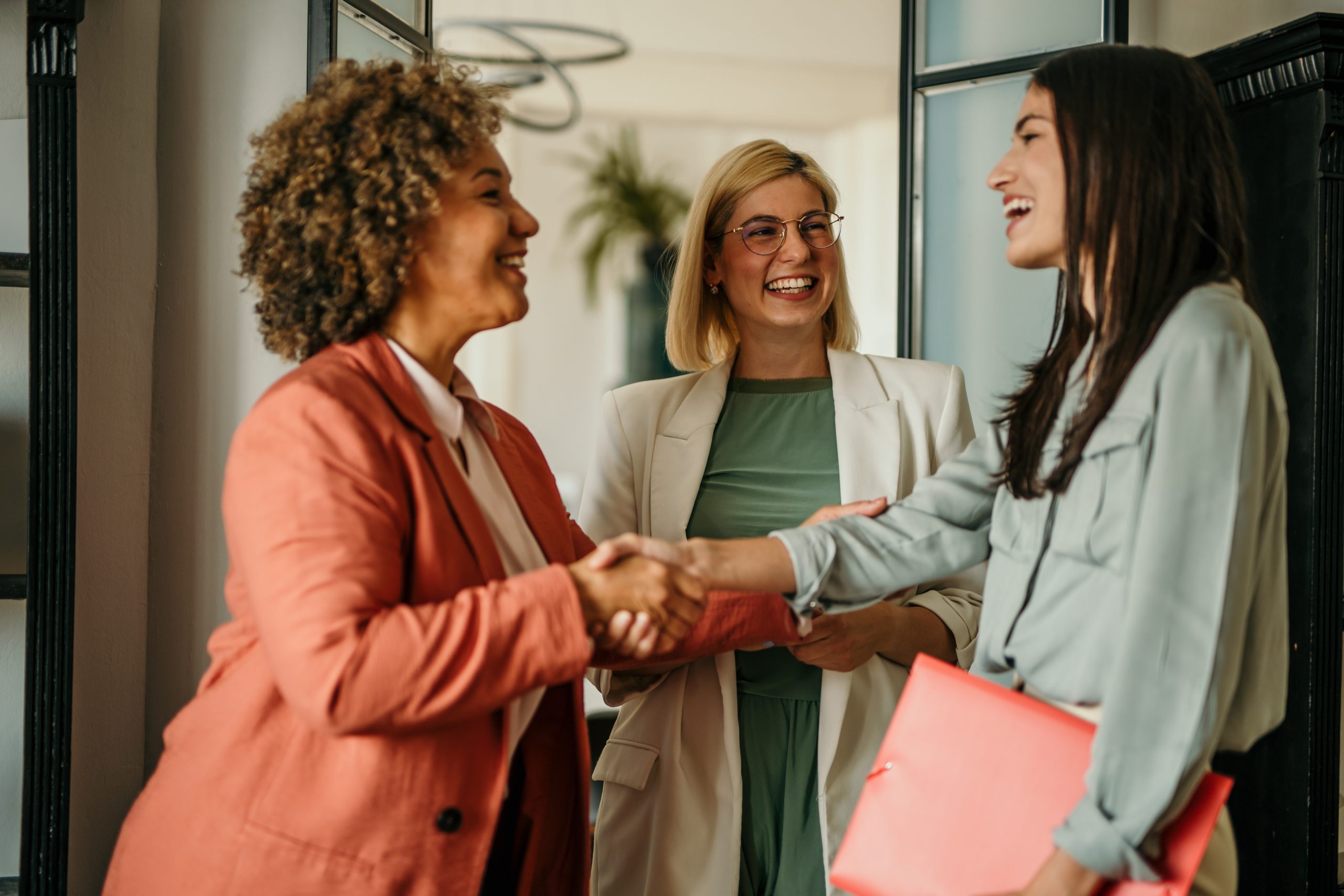 Three women meeting and shaking hands in office.